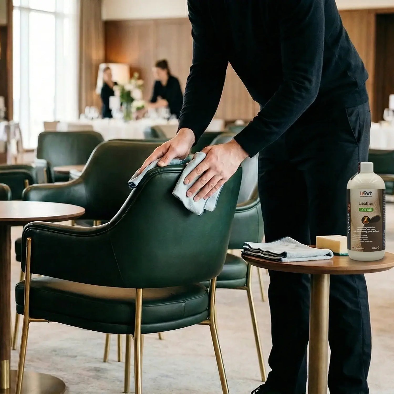 Person cleaning a green chair in a restaurant setting with a bottle of cleaning product on a table. LeTech leather repair