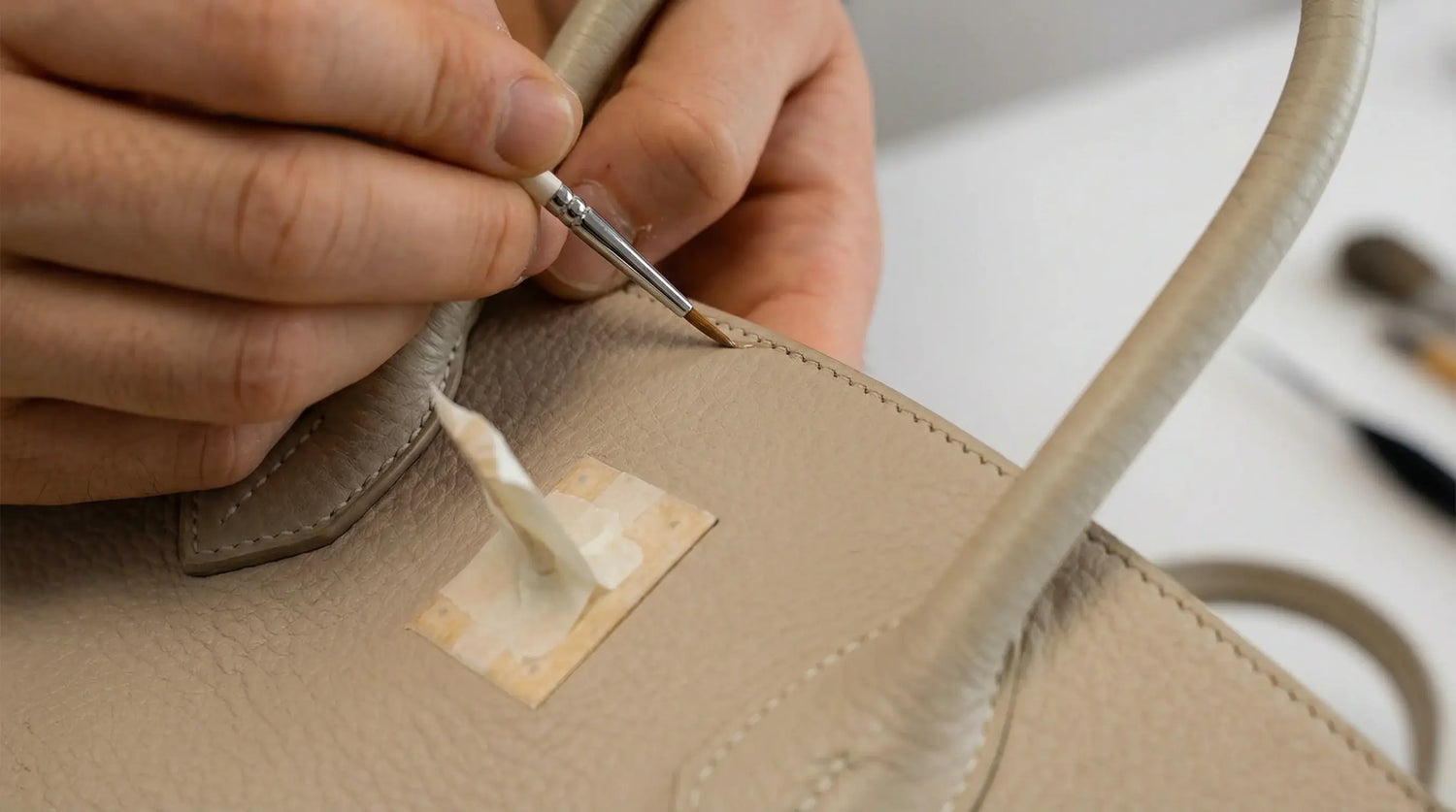 Person applying glue to a leather handbag with a visible brand label. LeTech leather repair