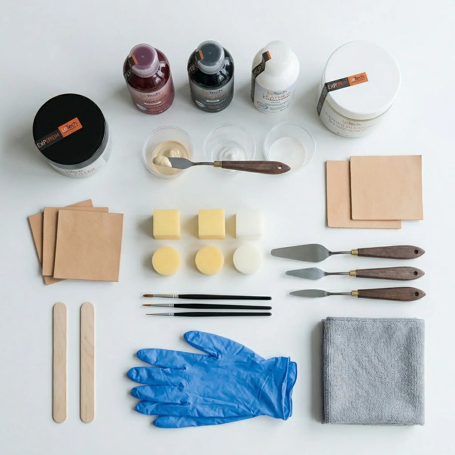 Assorted leather repair supplies by LeTech including bottles, containers, brushes, gloves, and paper on a white surface.