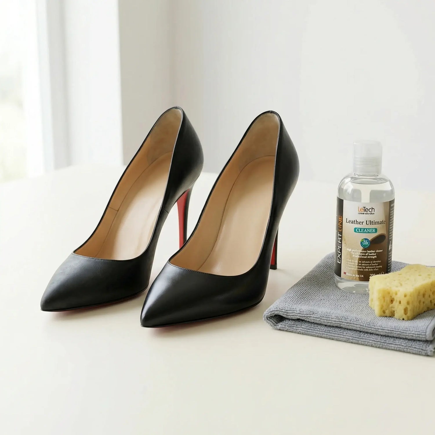 Black high-heeled shoes with a cleaning product and sponge on a white surface. Shoe leather repair by LeTech